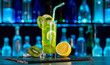Cocktail with kiwi, lemon, ice on bar counter in a restaurant, pub. Fresh prepared alcoholic cooler beverage at nightclub. Showcases with bottles on dark background