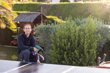 Young woman technician working in the installation of solar panels on the roof with electric screwdriver on hand