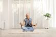 Man in jeans seated on a carpet doing yoga in a living room