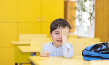 Preschooler Boy Is Crying Sitting On School Desk. Angry Unhappy Sad Upset Kid Don't Want To Go Back To School, Refuse.tears On Cheeks One Hand Cover Eye.backpack On Table.education First Day Alone