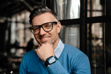 Adult handsome smiling man in glasses touching his chin