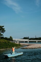 Poster - Fisherman in small boat departs from shore the background of highway passing through the river