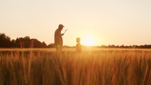 Farmer And His Son In Front Of A Sunset Agricultural Landscape. Man And A Boy In A Countryside Field. Fatherhood, Country Life, Farming And Country Lifestyle.