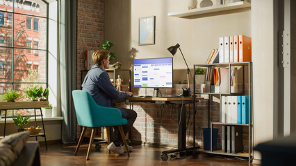 Fototapete - Remote Work Concept: Man Using Desktop Computer With Office Software to Check Schedule in Calendar. Young Male Planning Business Meetings in Stylish Loft Apartment with Big Window.