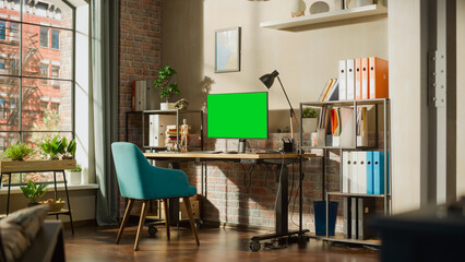 Fototapete - Desktop Computer Monitor Standing on Height Adjustable Desk with a Green Screen Chromakey Mock Up Display. Cozy Empty Loft Apartment with a Lamp, Notebooks and Smartphone on the Table.