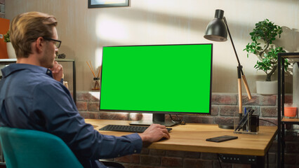 Poster - Young Handsome Man Working from Home on Desktop Computer with Green Screen Mock Up Display. Creative Male Checking Social Media, Browsing Internet. Living Room in Bright Loft Apartment.
