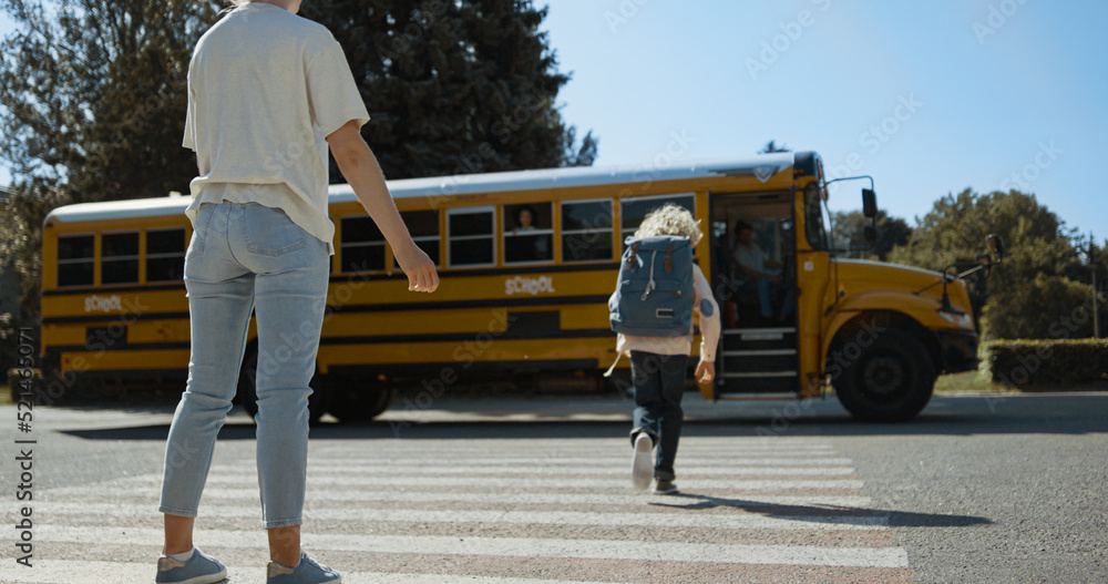 Mom give high five son escorting to schoolbus. Mother watch child boarding bus