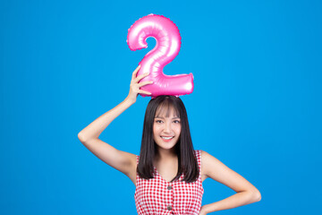 Happy new year and Merry Christmas concept. Beautiful young asian woman with balloons number 2 on blue background.