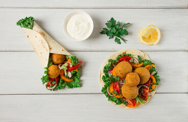 Wall Mural - Tortillas, wrapped falafel balls, with fresh vegetables, vegetarian healthy food, on a wooden white background, no people, selective focus.