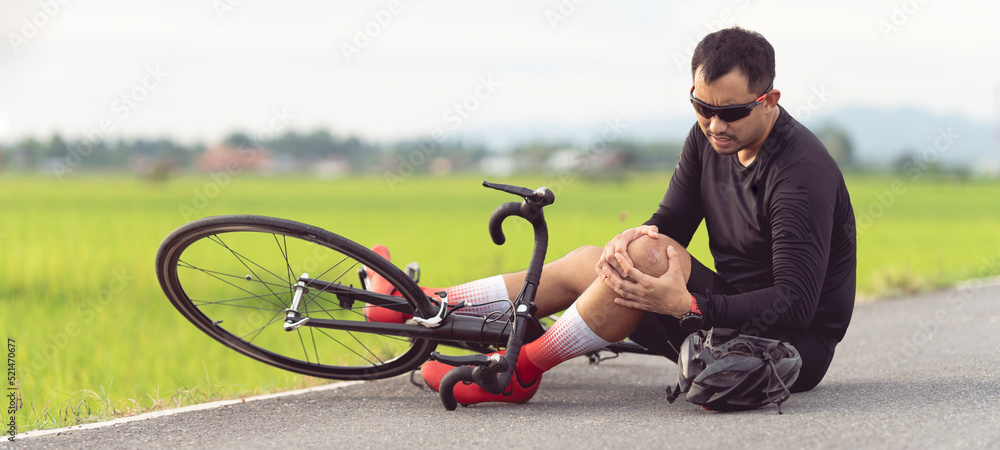 Bike injuries. Man cyclist fell fell off road bike while cycling. Bicycle accident injured knee. Road in Thailand. Stock Photo Adobe Stock