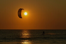 A Young Professional Kitesurfer Rides A Board Along The Surface Of The Sea At Sunset.