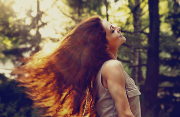 Wall Mural - Beautiful enjoying young woman relaxing with long healthy bright hair on nature bright sunny summer sunset yellow orange rays in the park trees background. Happy