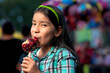 A happy girl eating caramel apple at a fair.