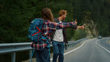 Fototapeta Natura - Two backpackers hitchhiking road. Couple tourists catch wait car in mountains.