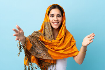 Canvas Print - Young Moroccan woman with traditional costume isolated on blue background presenting and inviting to come with hand