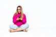 © luismolinero - Young caucasian woman sitting on the floor isolated on white background sending a message with the mobile