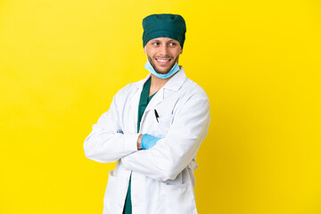 Wall Mural - Surgeon blonde man in green uniform isolated on yellow background with arms crossed and happy