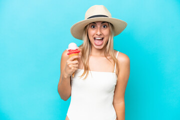 Young caucasian woman in swimsuit with a cornet ice cream isolated on blue background with surprise and shocked facial expression