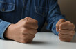 Man clenching fists at table while restraining anger, closeup