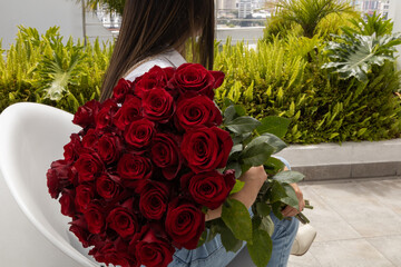 woman sitting on her back holding a large bouquet of red natural roses on a terrace, lifestyle and beauty of nature in the day, romantic gift