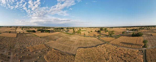 A beautiful 180 degree aerial panoram of wheat crop fields and mountains in the background and haystacks on the ground.