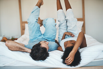 Wall Mural - Playful interracial couple bonding while lying on a bed in a bedroom in the morning. Loving, resting and relaxing diverse lovers enjoying quality time and being funny together in their broom at home