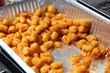 A view of a large aluminum foil container full of deep fried tater tots.