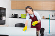 © Vitaliy - Young attractive housewife in red apron and yellow rubber gloves cleaning table with rag and bottle spray. Household and cleaning service concept