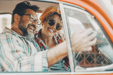 Happy couple having fun inside a car during travel adventure. Cheerful man and woman smiling and laughing a lot together. People enjoying vehicle trip in friendship and relationship. Concept of drive