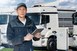 © scharfsinn86 - Fleet manager with a digital tablet stands next to electric trucks at electric vehicle charging stations