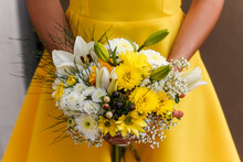 Close-Up Of A Bridesmaid In A Yellow Dress Holding A Bouquet Of Yellow And White Flowers
