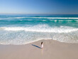 © AmazingAerialAgency - Aerial view of woman standing on beach in front of waves, Cape Town, South Africa.