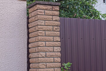 Sticker - part of a fence made of brown bricks and metal near a gray concrete wall on the street