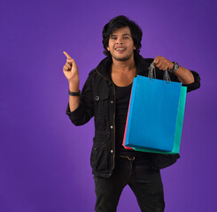 Wall Mural - Beautiful Indian young handsome man holding and posing with shopping bags on a purple background