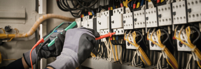 Electricity and electrical maintenance service, Engineer hand holding AC multimeter checking electric current voltage at circuit breaker terminal and cable wiring main power distribution board.