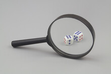 Dices Under Magnifying Glass On Gray Background. Gambling Review Concept.