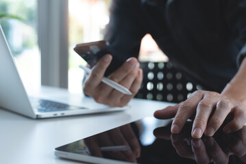 Business man using mobile phone and digital tablet, working on laptop computer at home office