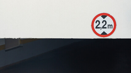 a red sign showing the height of the ceiling of 2.2 meters in the entrance to the underground parking on the white wall.