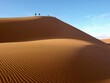 © Alice Makes - Huge big orange yellow sand dune in the desert in Namibia Africa with blue sky background and shadows on the sand walking tour expedition adventure group on top of dunes and footprints