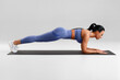 © nikolas_jkd - Fitness woman doing plank exercise on gray background. Athletic girl working out