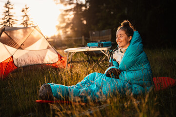 woman relaxing and lie in a sleeping bag in the tent. sunset camping in forest. mountains landscape 