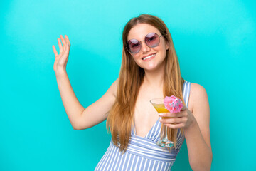 Wall Mural - Young woman isolated on blue background in swimsuit and holding a cocktail