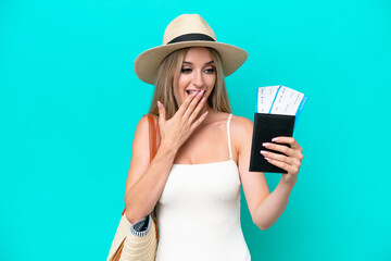 Blonde woman in swimsuit holding passport isolated on blue background with surprise and shocked facial expression