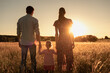 © kieferpix - Family of three standing in a meadow holding hands facing the sunset.