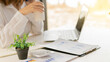 © ArLawKa - Young accountant holding coffee cup working on laptop with financial documents on desk in office