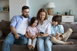 © fizkes - Young couple and preschoolers pretty children enjoy new mobile app using smartphone, make call or buying goods on-line, spend pastime on internet together resting on sofa at home. Modern tech concept