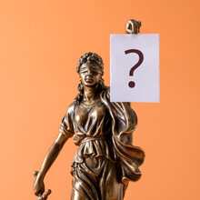 Statue Of Justice Themis Is A Symbol Of Law And Freedom And A White Sheet Of Paper Banner With A Question Mark. Minimal Creative Concept.