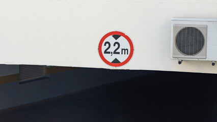 a red sign showing the height of the ceiling of 2.2 meters in the entrance to the underground parking on the white wall.