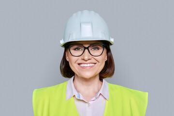 Female industrial worker in protective hard hat and vest on gray background