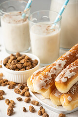 Close-up of two glasses of horchata with a straw, on a table with tiger nuts and fartons, white background, vertical